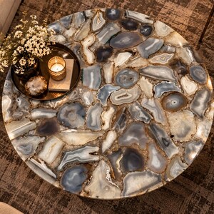 Peut inclure: Une table basse ronde avec un plateau compos&eacute; de nombreuses tranches d'agate polies et multicolores dans des tons de gris, bleu, blanc et marron. La surface est lisse et brillante, mettant en valeur les bandes concentriques naturelles.