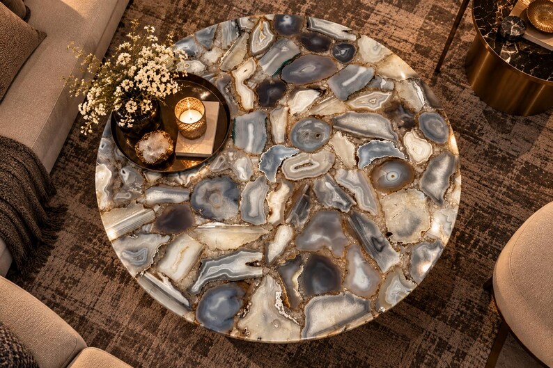 Peut inclure: Une table basse ronde avec un plateau compos&eacute; de nombreuses tranches d'agate polies et multicolores dans des tons de gris, bleu, blanc et marron. La surface est lisse et brillante, mettant en valeur les bandes concentriques naturelles.