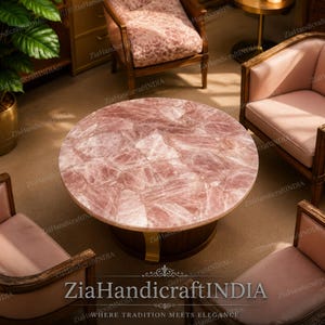 May include: A round coffee table with a rose quartz top. The table has a dark brown base with gold-colored metal accents. The table is surrounded by pink upholstered chairs.