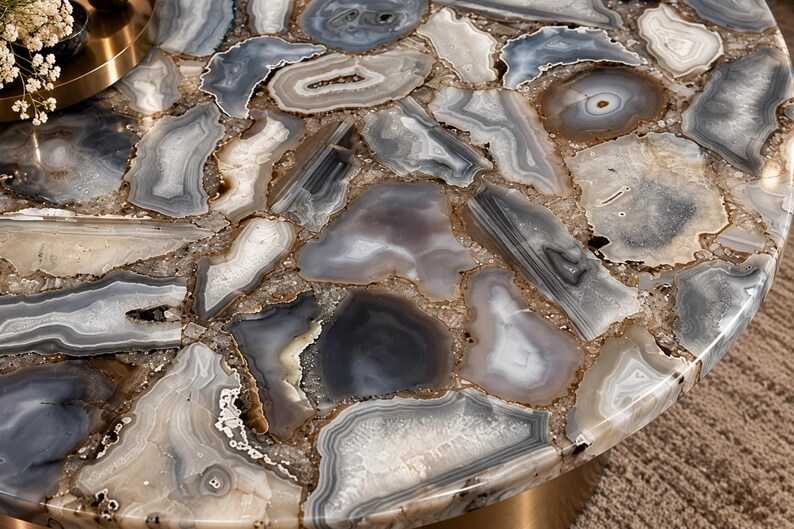 Peut inclure: Un plateau de table rond compos&eacute; d'une mosa&iuml;que de tranches d'agate polies grises, blanches et translucides. Les pierres sont dispos&eacute;es en un motif imbriqu&eacute; avec des textures cristallines et des bandes visibles, sous une surface lisse.