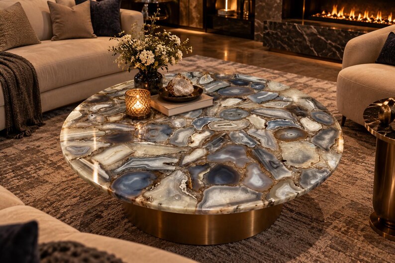 Peut inclure: Une table basse ronde avec un plateau compos&eacute; de tranches de pierre d'agate polies dans des tons bleus et blancs. La table repose sur une base cylindrique &agrave; la finition dor&eacute;e m&eacute;tallique, r&eacute;v&eacute;lant une mosa&iuml;que de motifs naturels.