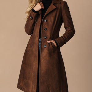 May include: A brown suede coat with a classic design. The coat features a notched collar, button closure, and pockets. The coat is knee-length and has a tailored fit. The coat is a rich, warm brown color.