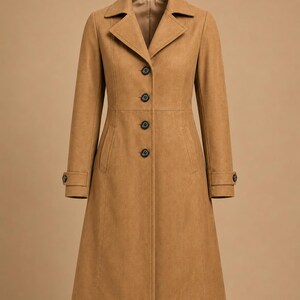 May include: A tan-colored coat with a classic design. The coat features a notched collar, four black buttons down the front, and two pockets. The long sleeves have buttoned cuffs. The coat is made of a soft, textured material.