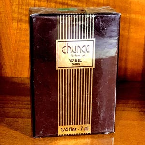 Op de afbeelding: Een rechthoekige parfumdoos in donkerbruin met verticale gouden krijtstrepen. Het midden bevat een wit label met de tekst chunga Parfum WEIL PARIS. De onderkant van de doos toont het volume als 1/4 fl oz - 7 ml in witte tekst.