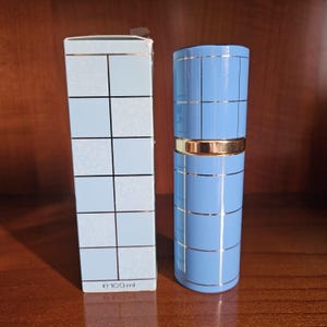 May include: A light blue rectangular perfume box and a matching cylindrical perfume bottle, both featuring a grid pattern of thin silver lines. The box displays the text e 100 ml at the bottom, and the bottle has a gold band at the center.