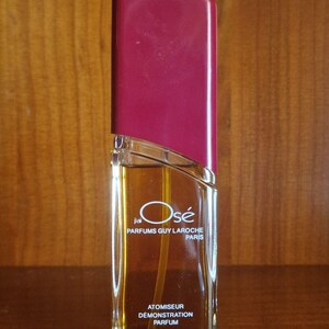 May include: A rectangular glass perfume bottle with a deep magenta cap. The bottle contains amber liquid and features the text J'ai Osé Parfums Guy Laroche Paris, Atomiseur Démonstration Parfum, 50 ml 3 77% vol 53 g printed on the front.