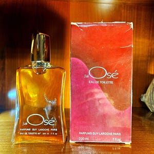 May include: A clear glass bottle of J'ai Osé Eau de Toilette by Parfums Guy Laroche Paris, containing 200 ml or 7 fl. oz of amber liquid, alongside its matching rectangular red and pink cardboard box featuring the same product name and volume.