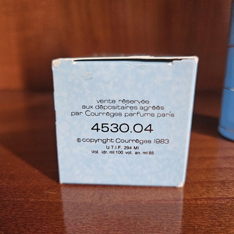 May include: A light blue rectangular perfume box with white text reading Vente r&eacute;serv&eacute;e aux d&eacute;positaires agr&eacute;&eacute;s par Courr&egrave;ges parfums paris, 4530.04, copyright Courr&egrave;ges 1983, U.T.I.F. 294 MI, Vol. idr. ml 100 vol. an. ml 85 printed on the front.