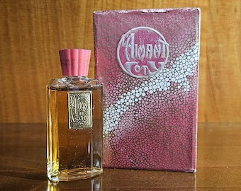 May include: A rectangular glass perfume bottle with a pink cap and a gold label reading Aimant de Coty, accompanied by a matching rectangular box featuring a textured pink and white dotted pattern and a circular logo with the text Aimant de Coty.