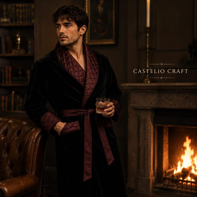 May include: A black velvet robe featuring a quilted burgundy shawl collar and matching quilted cuffs. The robe includes a tie belt at the waist. The text CASTELIO CRAFT is visible on the right side. The robe is worn by a person holding a glass.