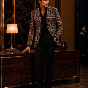Könnte beinhalten: Ein Blazer mit braun-schwarzem Leopardenmuster, getragen über einem einfarbigen schwarzen Hemd und einer schwarzen Hose. Das Outfit wird durch schwarze Lederschuhe und eine Armbanduhr mit weißem Zifferblatt und dunklem Lederarmband ergänzt.