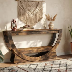 May include: A dark brown wooden console table with a curved base and a lower shelf. The table is decorated with a vintage lantern, books, and a vase with dried plants. A macrame wall hanging is above the table.