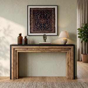 May include: A rectangular console table featuring a natural wood grain finish with tiered side supports and a solid black top. The table is adorned with two amber glass bottles, a small stack of books, a metallic hand sculpture, and a lamp.