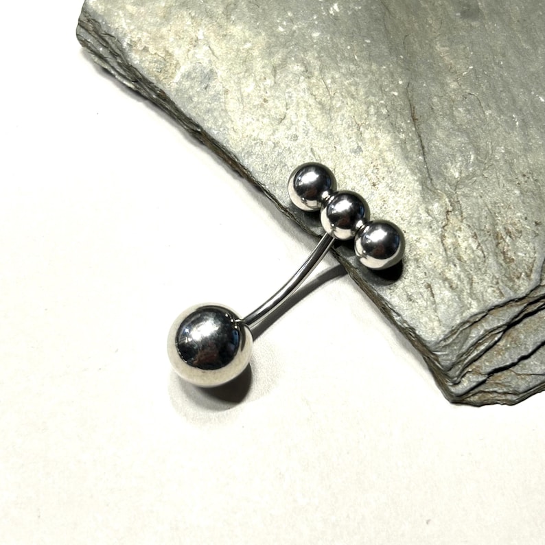 Puede incluir: Un broche plateado con un dise&ntilde;o &uacute;nico. El broche presenta cuatro formas esf&eacute;ricas: una esfera grande conectada a tres esferas m&aacute;s peque&ntilde;as por varillas met&aacute;licas finas y curvas. El broche se muestra sobre una superficie de piedra gris texturizada.