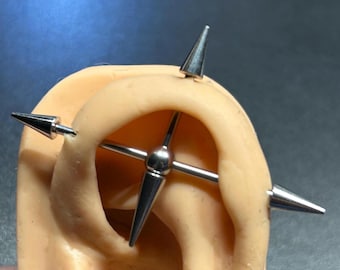 May include: A silver industrial barbell earring with four conical spikes and a central sphere. The earring is displayed on a tan ear model, showcasing the design and fit of the jewelry.