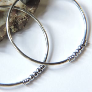 May include: Two silver bangle bracelets, one with a row of small silver beads. The bracelets are stacked on top of each other.