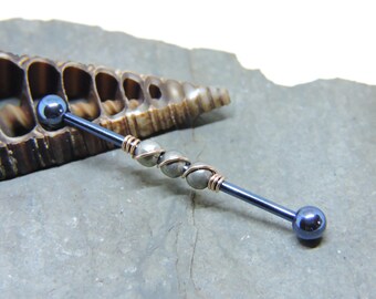 May include: A black industrial barbell with three silver beads wrapped in copper wire. The barbell is on a gray stone surface.