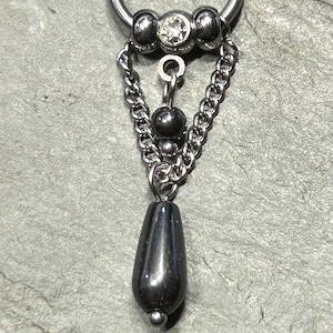 May include: A silver-toned captive bead ring featuring a central clear gemstone flanked by two metal beads. Two delicate silver chains drape downward, connecting to a central dark, teardrop-shaped pendant bead suspended by a small metal ring.