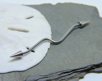 May include: A silver curved barbell with pointed ends. The barbell is lying on a white and gray surface.