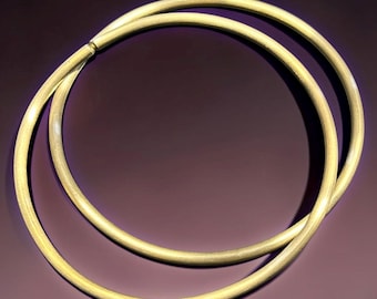 May include: Two circular gold-toned metal bangles with a brushed, matte texture. The bangles are thin, rounded, and feature a simple, continuous design. They are positioned overlapping each other, showcasing a consistent metallic finish throughout.
