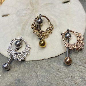 May include: Three belly button rings featuring a straight barbell with a spherical end and a circular hoop attachment. The hoops are adorned with intricate scrollwork patterns. The set includes one silver-tone, one gold-tone, and one rose gold-tone piece.