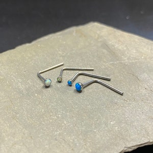 May include: Four silver nose rings with opal stones. Two of the rings have white opal stones and two have blue opal stones.