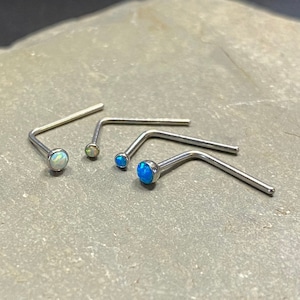 May include: Three silver nose rings with opal stones. The stones are blue and white.