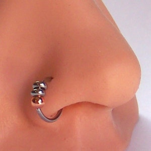 Può includere: Un anello per il naso in argento con tre perline. Le perline sono in argento, oro rosa e argento.
