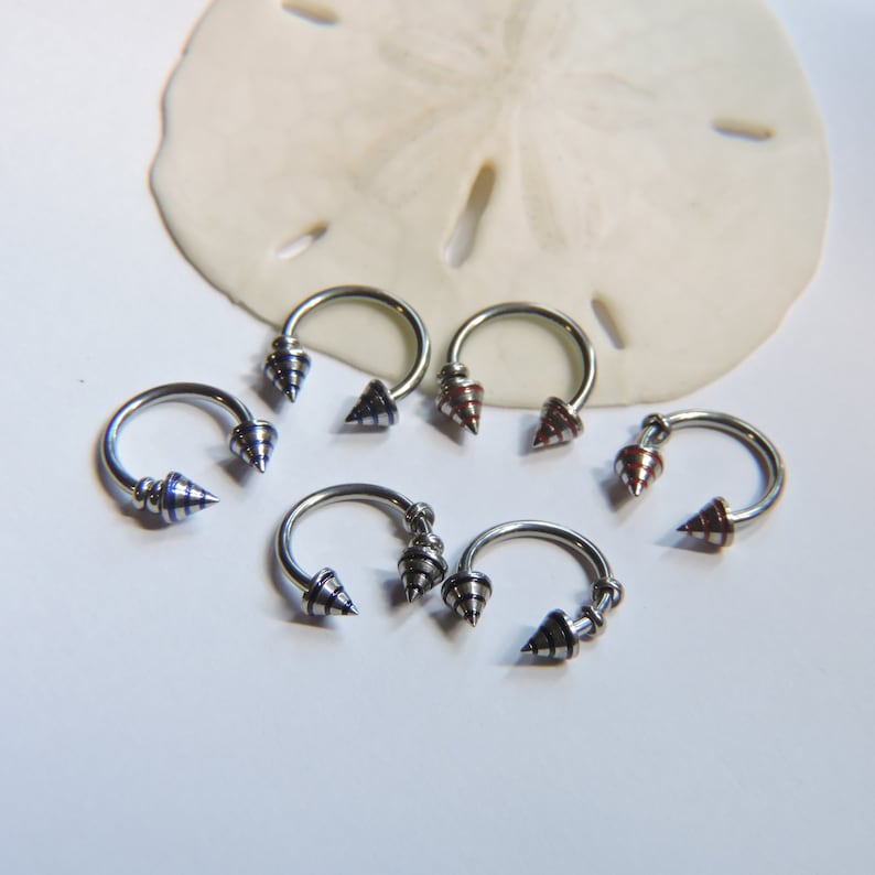 May include: Five silver circular horseshoe-shaped rings with pointed ends. The points are decorated with blue, red, and white stripes.