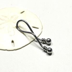 May include: A silver-toned metal body jewelry piece featuring a curved, twisted bar design that forms a loop at one end. The two ends of the bar are finished with polished spherical beads, each accented by a small grooved ring detail near the base.