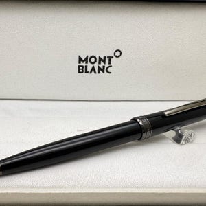 Op de afbeelding: Een zwarte Montblanc pen in de originele doos. De pen heeft een slanke, glanzende afwerking met zilverkleurige accenten. Het Montblanc logo is zichtbaar op de doos.
