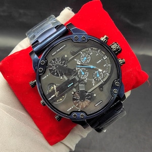 Könnte beinhalten: Eine dunkelblaue, übergroße Armbanduhr mit einem Multi-Zifferblatt, das drei verschiedene Zeitzonen mit der Beschriftung Time 1, Time 2 und Time 3 anzeigt. Das Zifferblatt enthält den Text Only The Brave, 3 Bar und DZ7414 mit blauen Akzenten.