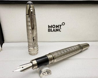 May include: A silver Montblanc fountain pen with a black grip and a silver nib, presented in its box. The pen features a textured, grid-like pattern on the barrel and cap. The Montblanc logo is visible on the box.