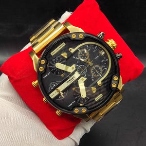 Könnte beinhalten: Eine goldfarbene Diesel-Armbanduhr aus Edelstahl mit einem großen schwarzen Zifferblatt, mehreren Hilfszifferblättern sowie goldenen Zeigern und Indizes. Das Zifferblatt zeigt den Text ONLY THE BRAVE, DIESEL, 3 BAR und DZ7333 sowie vier Zeitzonen.
