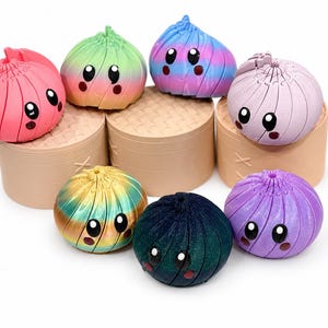 May include: A collection of seven small, round, articulated dumpling-shaped figures with cartoon faces, each featuring a unique color gradient or solid finish. The figures are arranged on top of three cylindrical, tan-colored bamboo steamer baskets.