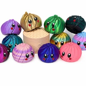 May include: A collection of eleven spherical, dumpling-shaped figurines with smooth, metallic, and iridescent finishes in various colors including purple, gold, green, black, blue, and pink, each featuring large black eyes and small red circular cheeks.