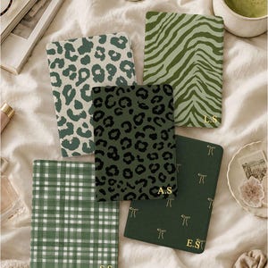 Puede incluir: Cinco cuadernos rectangulares con patrones en verde y blanco, incluyendo estampado de leopardo, rayas de cebra, cuadros y motivos de lazos. Tres cuadernos tienen iniciales doradas: L.S, A.S y E.S, mientras que uno tiene S.S. Las portadas tienen tonos verdes.