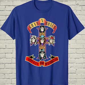 May include: A royal blue short-sleeve t-shirt featuring a graphic print of a purple cross with five skulls. The text Guns N' Roses appears on a red banner above, and Appetite For Destruction is printed on a red banner below the cross design.
