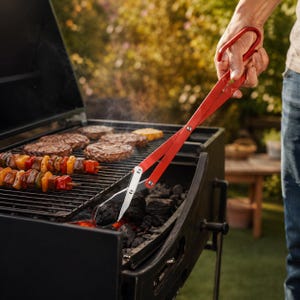 Peut inclure: Une paire de pinces à charbon en métal rouge à long manche avec des embouts en métal argenté. Les pinces présentent un mécanisme de type ciseaux et une poignée incurvée, positionnées au-dessus d'un barbecue à charbon noir avec des braises.