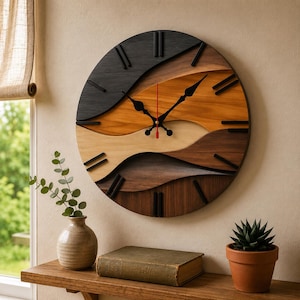 Op de afbeelding: Een ronde houten wandklok met een gelaagd ontwerp in tinten zwart, bruin en beige. De klok heeft zwarte wijzers en uurmarkeringen, met een rode secondewijzer. De klok heeft een diameter van ongeveer 46 cm.