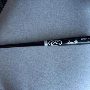 May include: A black Rawlings baseball bat with silver accents and a signature. The bat has the Rawlings logo and the word "PRO" printed on it. The bat is lying on a gray surface.