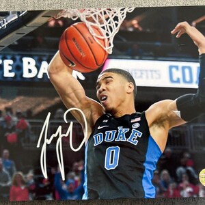 May include: A signed photograph of a basketball player in a Duke jersey, mid-dunk. The player is wearing a black and blue jersey with the word "DUKE" and the number "0" visible. The basketball is orange, and the net is white.