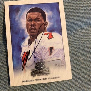 Könnte beinhalten: Eine 2002 Gridiron Kings by Donruss Sport-Sammelkarte mit einer Illustration von Michael Vick in einem weißen Atlanta Falcons Trikot mit der Nummer 7. Die Karte enthält ein Autogramm in schwarzer Tinte und den Text Michael Vick QB Falcons.
