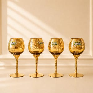 Peut inclure: Quatre verres à pied en verre ambré avec des tiges torsadées dorées et des bases circulaires. Chaque calice présente un motif complexe en filigrane doré et un motif floral peint à la main avec des pétales blancs et bleus et des feuilles vertes.