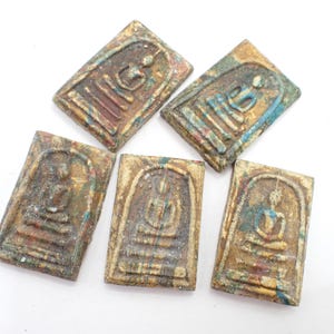May include: Five rectangular, weathered Buddha amulets. Each amulet features a seated Buddha figure within a rectangular frame. The amulets have a mottled appearance with colors of brown, gold, blue, and red. The background is white.