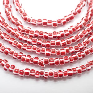 May include: A strand of red and white striped glass beads. The beads are small and round, and they are strung together on a clear thread.