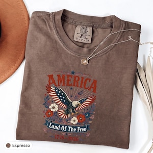 Camiseta Comfort Colors® America Land Of The Free 1776 2026 com estampa floral e águia, ideal para presente de aniversário. Peso pesado.