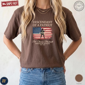 Pode incluir: Uma t-shirt castanha de manga curta com o texto Descendant of a Patriot sobre um gr&aacute;fico de uma bandeira americana e a silhueta de um soldado. Abaixo da bandeira, o texto diz Pvt. Thomas Blackwell, Pennsylvania Line, 3rd Battalion, 1777-1783.