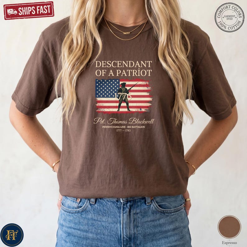 Pode incluir: Uma t-shirt castanha de manga curta com o texto Descendant of a Patriot sobre um gr&aacute;fico de uma bandeira americana e a silhueta de um soldado. Abaixo da bandeira, o texto diz Pvt. Thomas Blackwell, Pennsylvania Line, 3rd Battalion, 1777-1783.