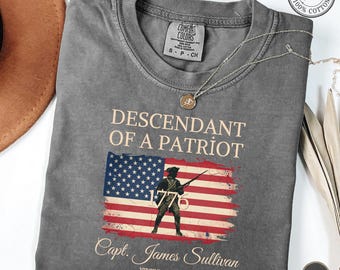 Op de afbeelding: Een antracietgrijs t-shirt met korte mouwen met de tekst Descendant of a Patriot boven een afbeelding van een soldaat die een geweer vasthoudt voor een Amerikaanse vlag. Onder de vlag staat de tekst Capt. James Sullivan Virginia Militia 1775-1783.